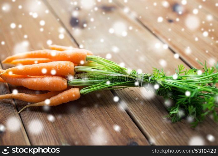 healthy eating, food, diet and vegetarian concept - close up of carrot bunch on wooden table over snow. close up of carrot bunch on wooden table