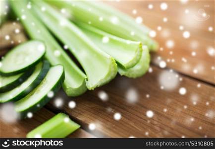 healthy eating, food, diet and vegetarian concept - close up of green celery stems and sliced cucumber on wood over snow. close up of celery stems and sliced cucumber