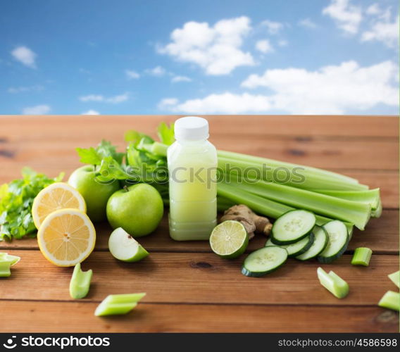 healthy eating, food, dieting and vegetarian concept - bottle with green juice, fruits and vegetables on wooden table over blue sky background