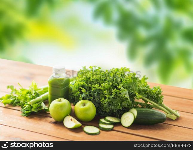 healthy eating, food, dieting and vegetarian concept - bottle with green juice, fruits and vegetables on wooden table over natural background. close up of bottle with green juice and vegetables. close up of bottle with green juice and vegetables