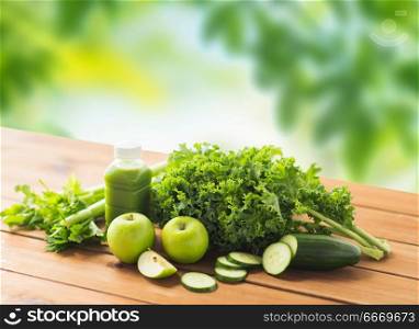 healthy eating, food, dieting and vegetarian concept - bottle with green juice, fruits and vegetables on wooden table over natural background. close up of bottle with green juice and vegetables. close up of bottle with green juice and vegetables