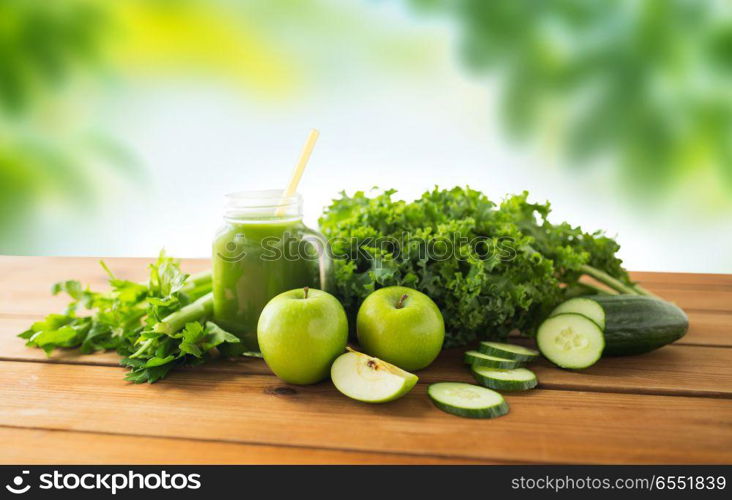 healthy eating, food, dieting and vegetarian concept - close up of glass mug or mason jar with green juice, fruits and vegetables on wooden table over natural background. mason jar with juice and green vegetable food. mason jar with juice and green vegetable food