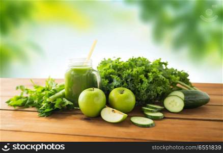 healthy eating, food, dieting and vegetarian concept - close up of glass mug or mason jar with green juice, fruits and vegetables on wooden table over natural background. mason jar with juice and green vegetable food. mason jar with juice and green vegetable food