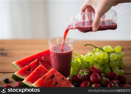 healthy eating, food, dieting and vegetarian concept - close up of hand pouring fruit and berry juice or smoothie from bottle to glass