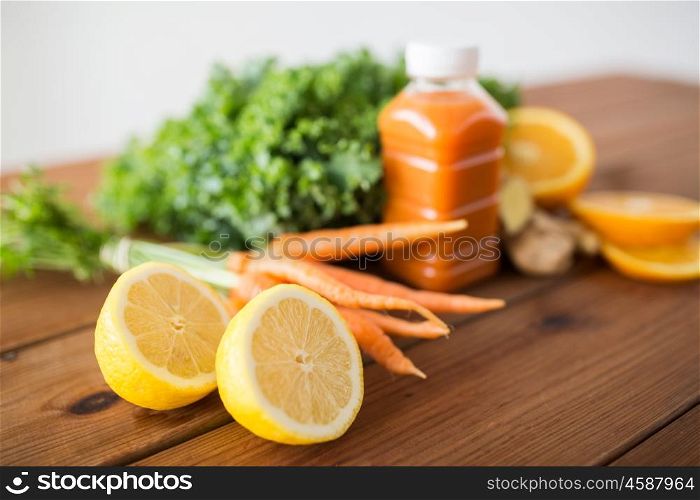 healthy eating, food, dieting and vegetarian concept - close up of lemon and bottle with carrot juice, fruits and vegetables on wooden table