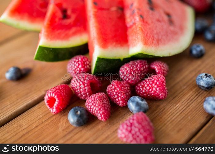 healthy eating, food, dieting and vegetarian concept - close up of raspberry, blackberry and watermelon slices on wooden table