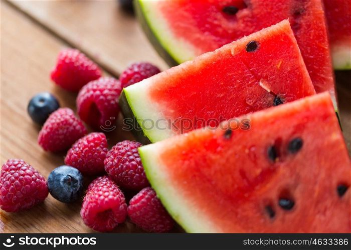 healthy eating, food, dieting and vegetarian concept - close up of raspberry, blueberry and watermelon slices on wooden table
