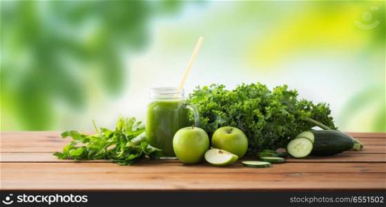 healthy eating, food, dieting and vegetarian concept - glass jug or mug with green juice, fruits and vegetables on wooden table over green natural background. close up of jug with green juice and vegetables. close up of jug with green juice and vegetables