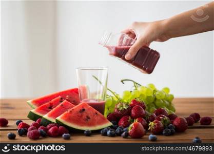 healthy eating, food, dieting and vegetarian concept - hand pouring fruit and berry juice or smoothie from bottle to glass