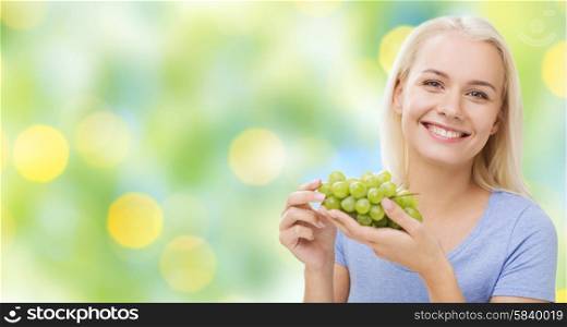 healthy eating, food, fruits, diet and people concept - happy woman eating grapes over summer green holidays lights background