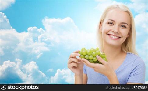 healthy eating, food, fruits, diet and people concept - happy woman eating grapes over blue sky and clouds background