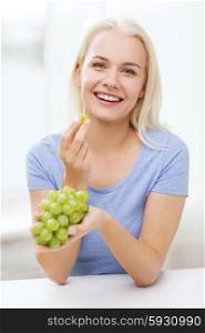 healthy eating, food, fruits, diet and people concept - happy woman eating grapes at home
