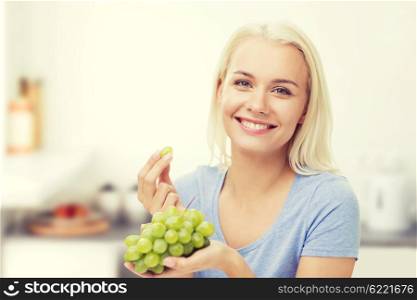 healthy eating, food, fruits, diet and people concept - happy woman eating grapes over kitchen background
