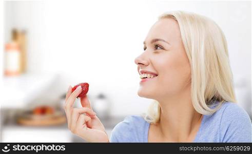 healthy eating, food, fruits, diet and people concept - happy woman eating strawberry over kitchen background