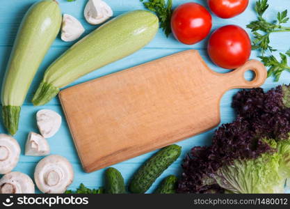 healthy eating. fresh vegetables on a blue wooden background. zucchini, mushrooms, tomatoes, cucumber, herbs, salad and cutting board