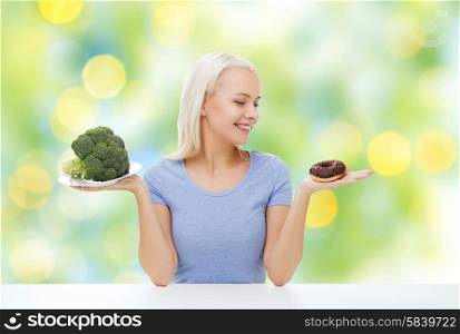 healthy eating, junk food, diet and choice people concept - smiling woman choosing between broccoli and donut over summer green holidays lights background