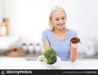 healthy eating, junk food, diet and choice people concept - smiling woman choosing between broccoli and donut over kitchen background