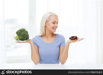 healthy eating, junk food, diet and choice people concept - smiling woman choosing between broccoli and donut at home