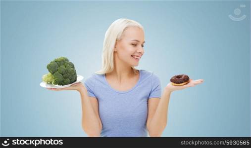 healthy eating, junk food, diet and choice people concept - smiling woman choosing between broccoli and donut over blue background