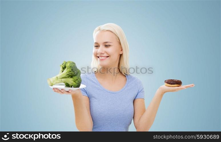 healthy eating, junk food, diet and choice people concept - smiling woman choosing between broccoli and donut over blue background