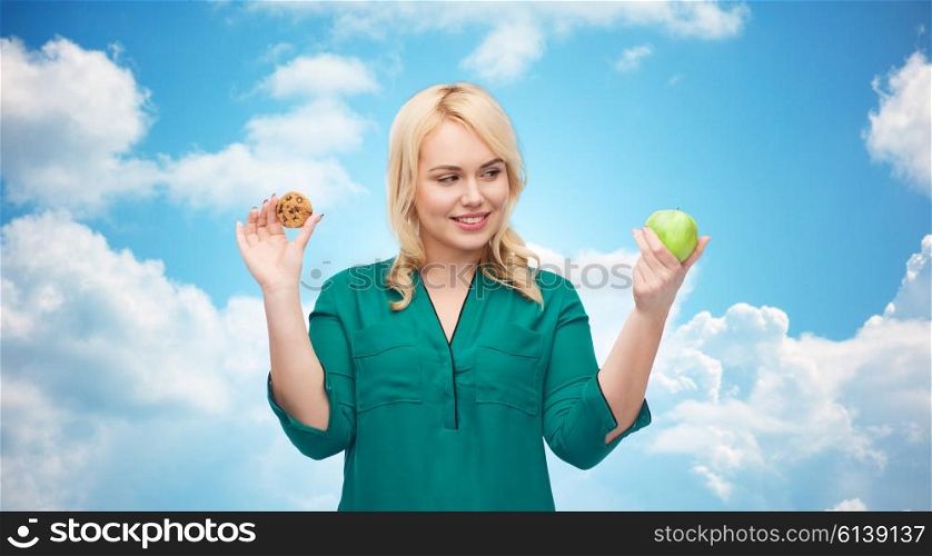 healthy eating, junk food, diet and choice people concept - smiling woman choosing between apple and cookie over blue sky and clouds background