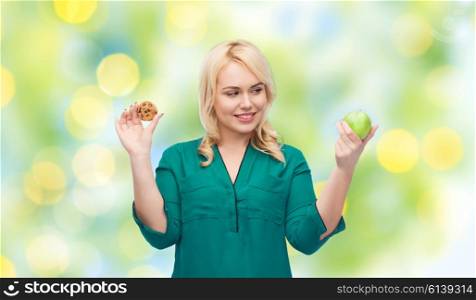 healthy eating, junk food, diet and choice people concept - smiling woman choosing between apple and cookie over green lights background