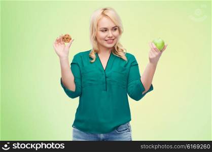 healthy eating, junk food, diet and choice people concept - smiling woman choosing between apple and cookie over green natural background