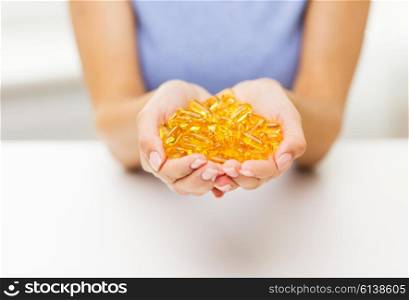 healthy eating, medicine, health care, food supplements and people concept - close up of woman hands holding pills or fish oil capsules at home