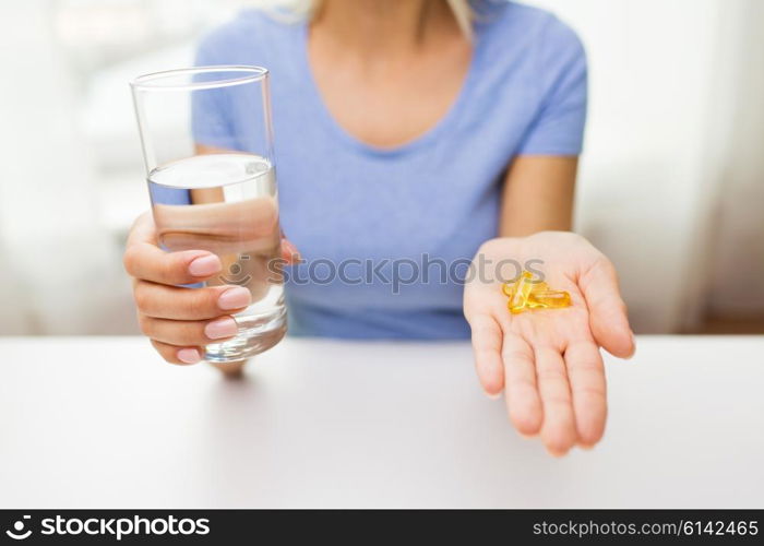 healthy eating, medicine, health care, food supplements and people concept - close up of woman hands holding pills or fish oil capsules and water glass at home