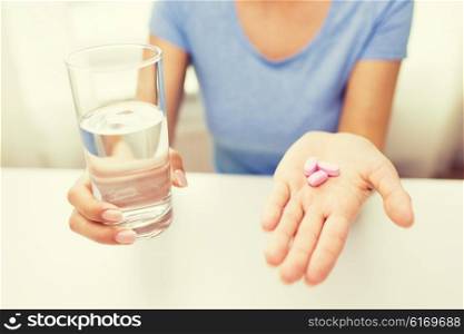 healthy eating, medicine, health care, food supplements and people concept - close up of woman hands holding pills and water glass at home