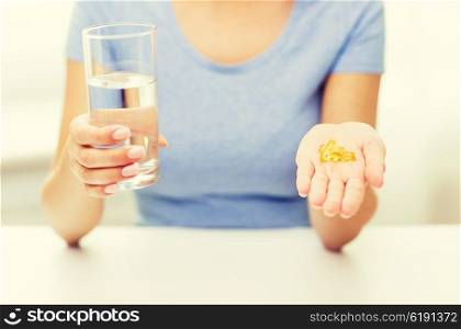 healthy eating, medicine, health care, food supplements and people concept - close up of woman hands holding pills or fish oil capsules and water glass at home