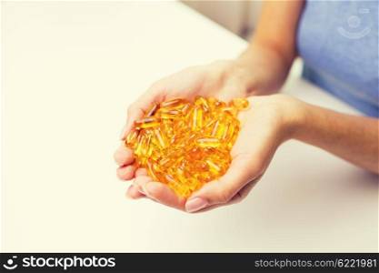 healthy eating, medicine, health care, food supplements and people concept - close up of woman hands holding pills or fish oil capsules at home
