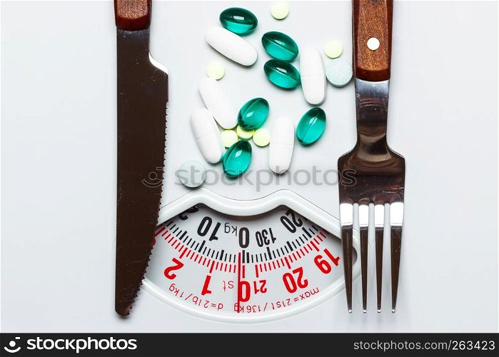 Healthy eating, medicine, health care, food supplements and weight loss concept. Pills with knife fork on dish white scales
