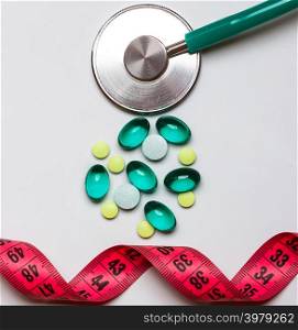 Healthy eating, medicine, health care, food supplements and weight loss concept. Pills with measuring tape and stethoscope on table