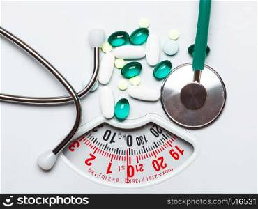 Healthy eating, medicine, health care, food supplements and weight loss concept. Pills with stethoscope on white scales