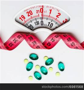 Healthy eating, medicine, health care, food supplements and weight loss concept. Pills with measuring tape on white scales