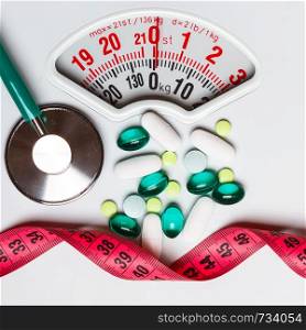 Healthy eating, medicine, health care, food supplements and weight loss concept. Pills with measuring tape and stethoscope on white scales