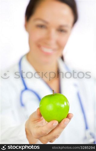 Healthy eating or lifestyle concept shot of a smiling woman doctor holding and offering a green apple, the focus is on the apple in the foreground.