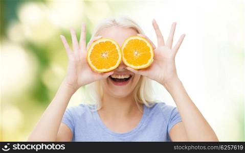 healthy eating, organic food, fruit diet, comic and people concept - happy woman having fun and covering her eyes with orange slices over green natural background