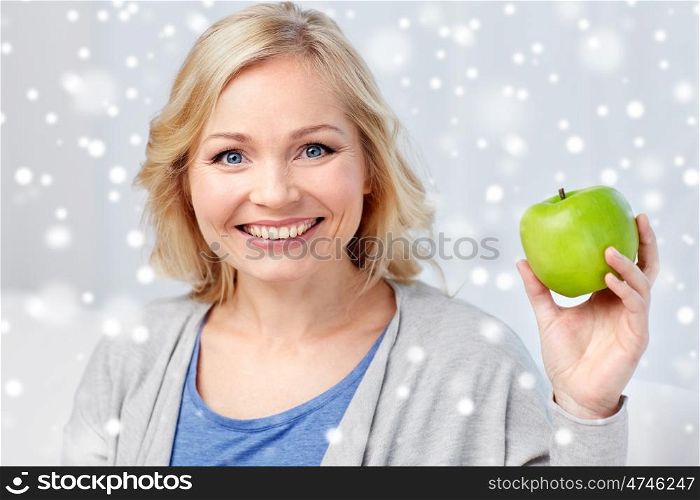 healthy eating, organic food, fruits, diet and people concept - happy middle aged woman with green apple at home over snow
