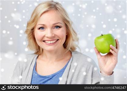 healthy eating, organic food, fruits, diet and people concept - happy middle aged woman with green apple at home over snow