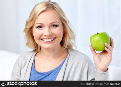 healthy eating, organic food, fruits, diet and people concept - happy middle aged woman with green apple at home