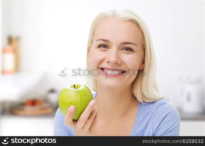 healthy eating, organic food, fruits, diet and people concept - happy woman eating green apple over kitchen background
