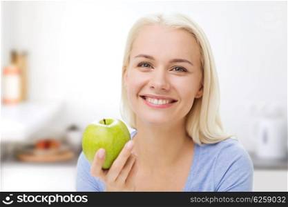 healthy eating, organic food, fruits, diet and people concept - happy woman eating green apple over kitchen background