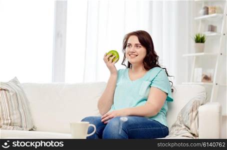 healthy eating, organic food, fruits, diet and people concept - happy young plus size woman eating green apple at home