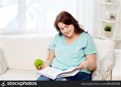 healthy eating, organic food, fruits, diet and people concept - happy young plus size woman reading book and eating green apple at home