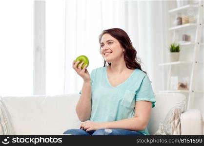 healthy eating, organic food, fruits, diet and people concept - happy young plus size woman eating green apple at home