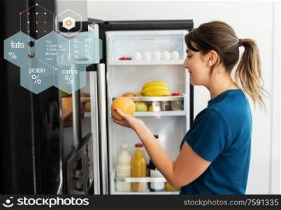 healthy eating, people and diet concept - happy woman taking grapefruit from fridge at home kitchen over food nutritional value chart. happy woman taking food from fridge at home