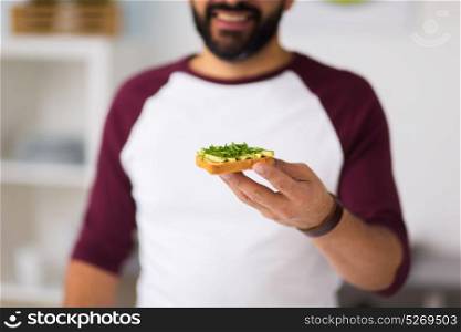 healthy eating, people and diet concept - man having avocado sandwich for breakfast at home kitchen. man eating avocado sandwich at home kitchen
