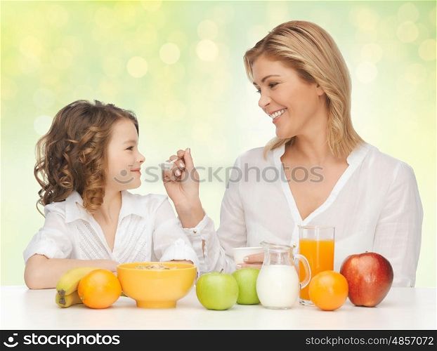 healthy eating, people, family and food concept - happy mother and daughter having breakfast over green holidays lights background